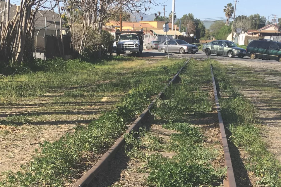 Old railroad line overgrown with grass with cars parked in background